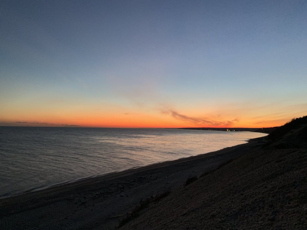 Orange sunset over Long Island Sound from a bluff above a curving beach