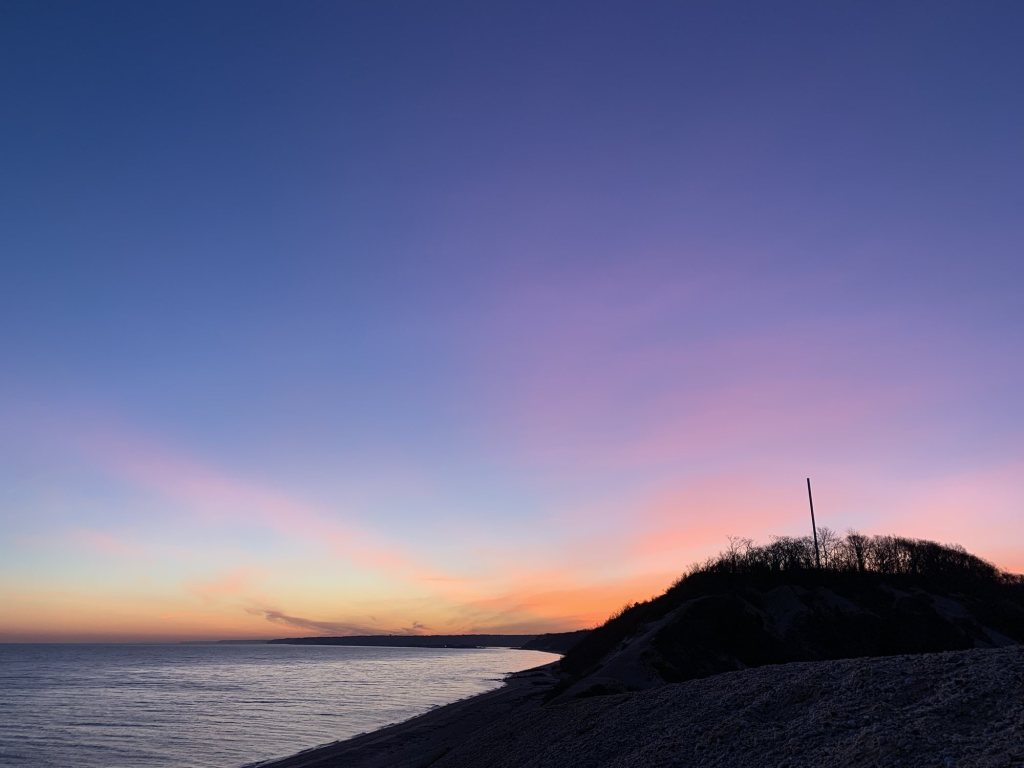 Pink and purple dusk sky over a bluff and beach on Long Island Sound