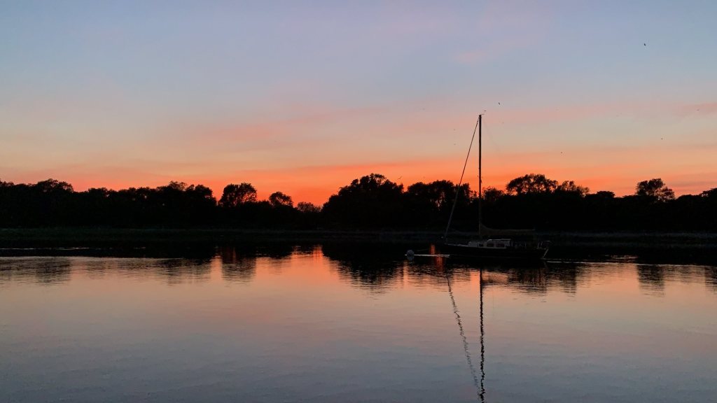 Sailboat moored in a calm harbor under an orange sunset