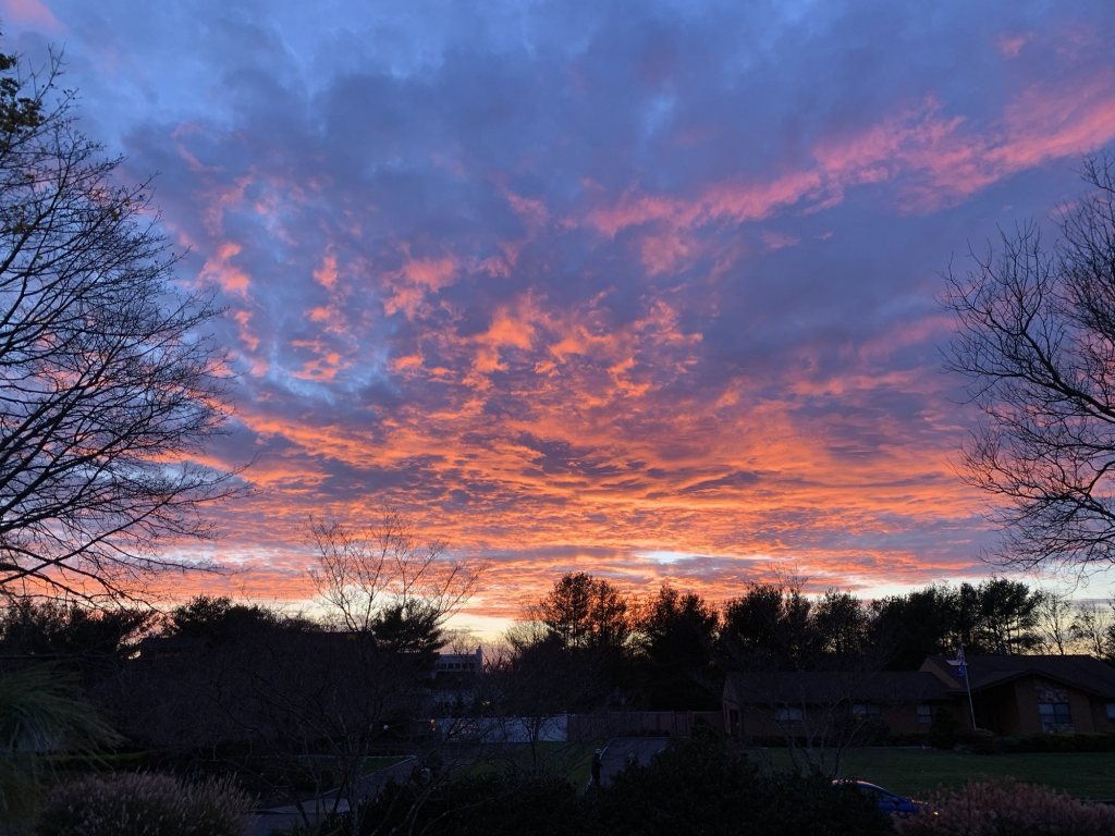 Fiery orange clouds filling the sky at sunset over a neighborhood