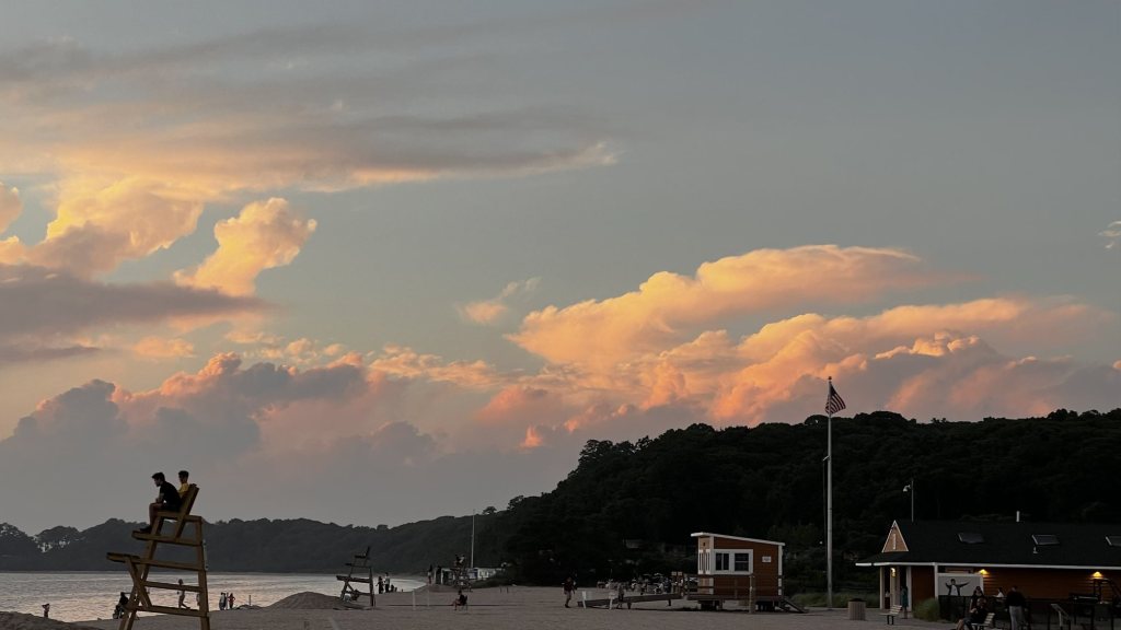 Pink sunset clouds over a beach with a lifeguard stand and flag