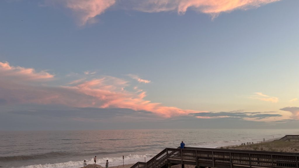Pink clouds over an ocean beach and boardwalk at sunset