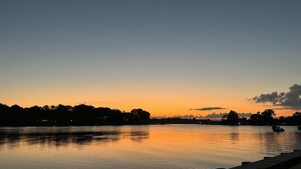 Orange sunset reflected in a calm harbor beside a dock