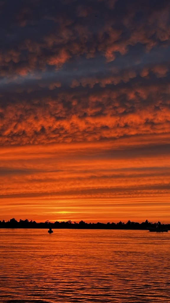 Fiery orange sunset over the water at West Meadow Beach, with a boat silhouetted on the horizon